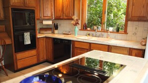 Une cuisine moderne avec des meubles en bois, un four noir, un lave-vaisselle, une cuisinière et une fenêtre donnant sur un paysage verdoyant.