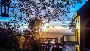 Une terrasse en bois avec une table et des chaises, donnant sur une étendue d’eau au coucher du soleil.