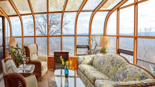 Une véranda meublée de mobilier en osier, avec une table basse en verre et une vue sur l’extérieur.