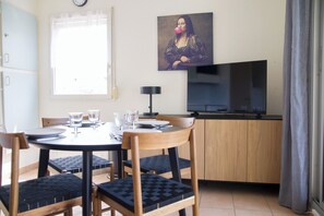 Een eetgedeelte met een ronde tafel, vier stoelen, een televisie en een schilderij aan de muur.