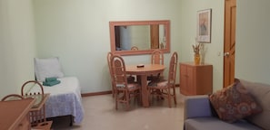 Une pièce de taille modeste comprenant un lit, une petite table avec des chaises, une table à manger avec des chaises, un miroir, un meuble et un canapé.