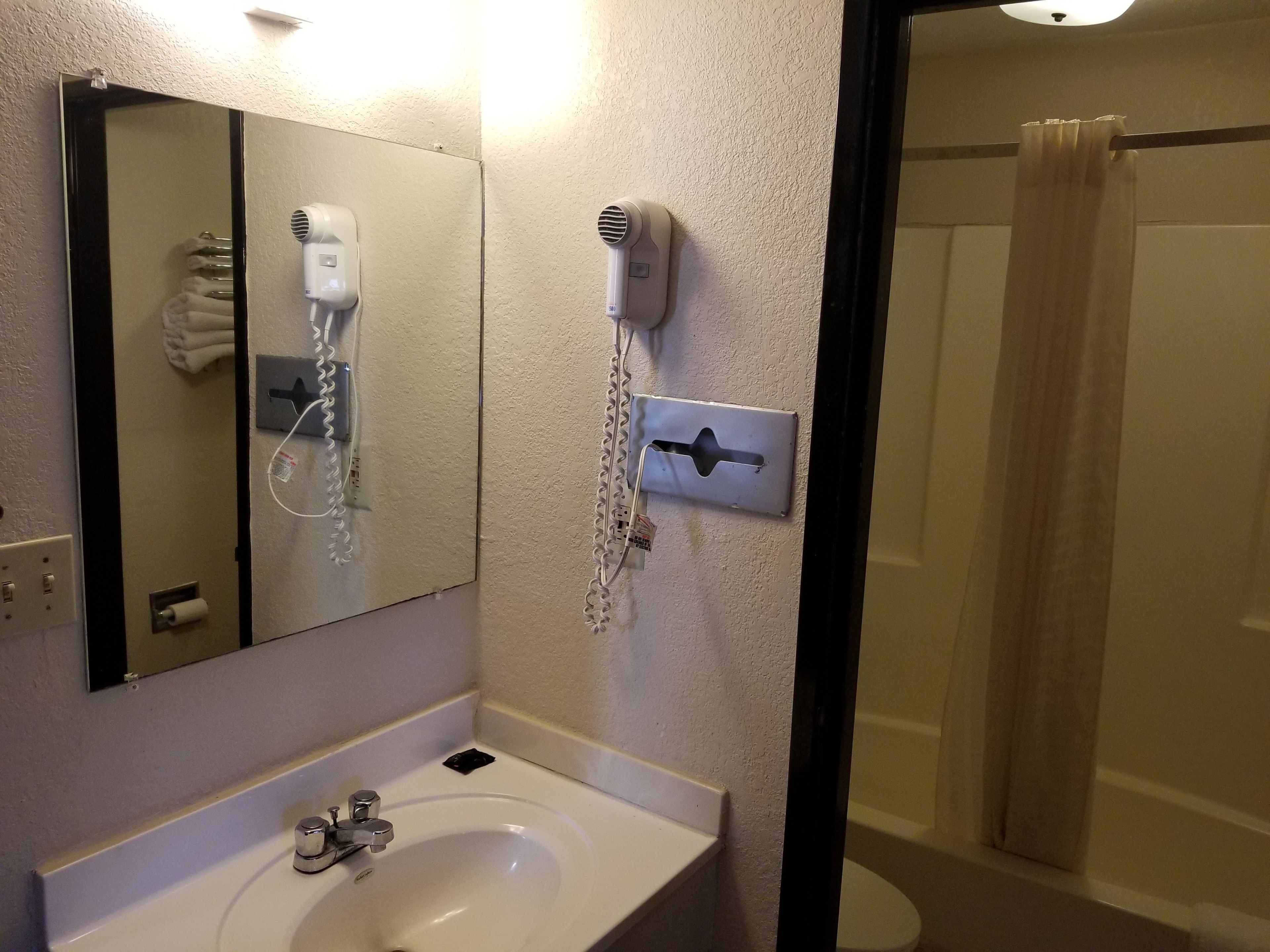 Un baño con lavamanos, espejo, secador de pelo y cortina de ducha.