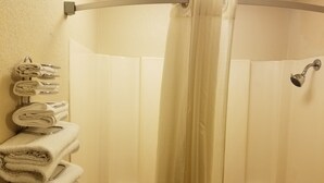 A bathroom with a shower curtain, a towel rack with folded towels, and a showerhead. - Americas Stay Inn (Leavenworth)