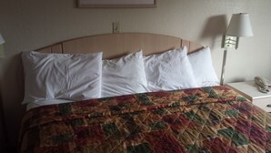 A hotel room with a bed, white pillows, a colorful quilt, a bedside lamp, and a phone on the nightstand. - Americas Stay Inn (Leavenworth)
