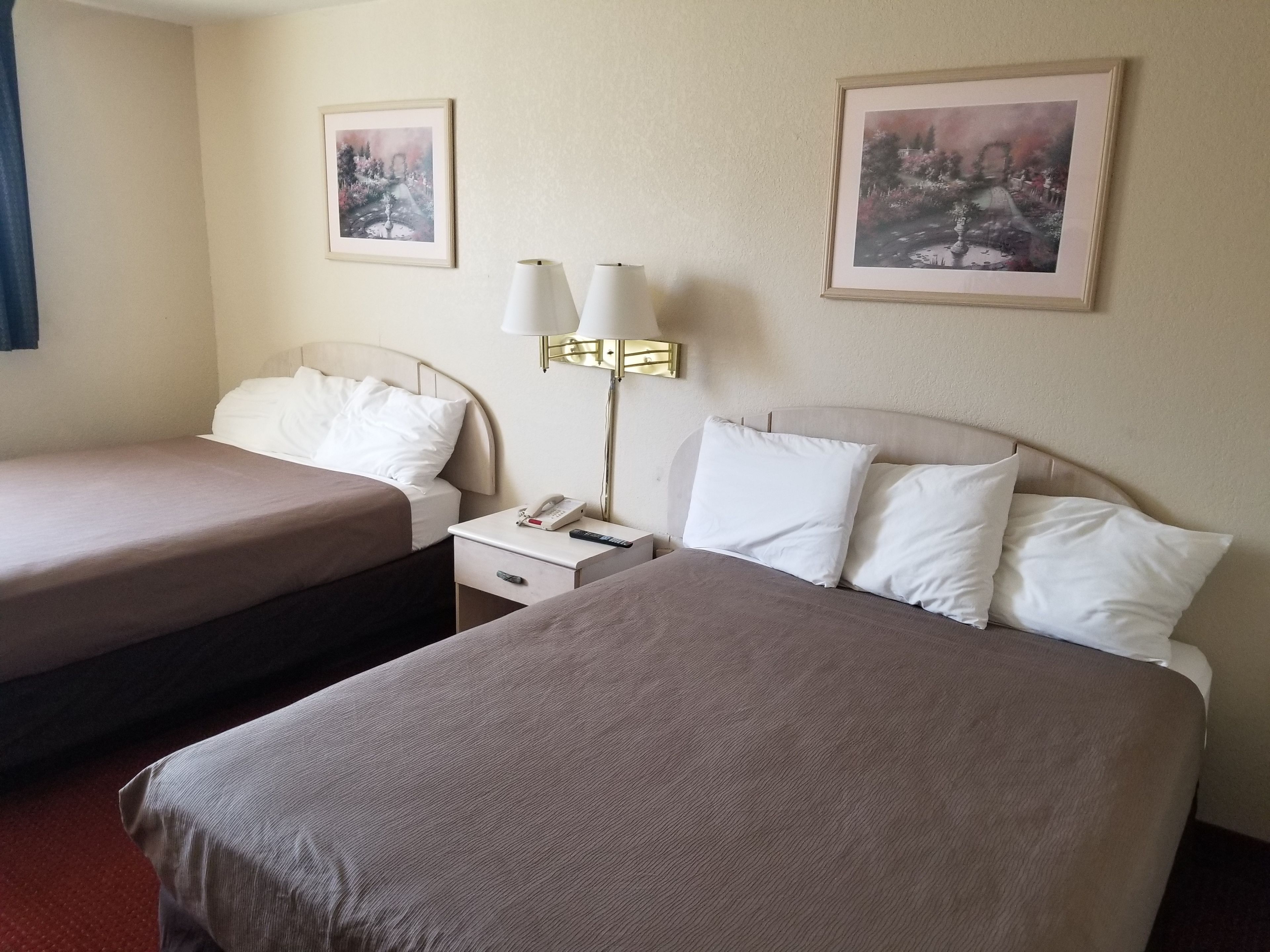 Una habitación de hotel con dos camas, una mesita de noche con una lámpara y dos cuadros enmarcados en la pared.