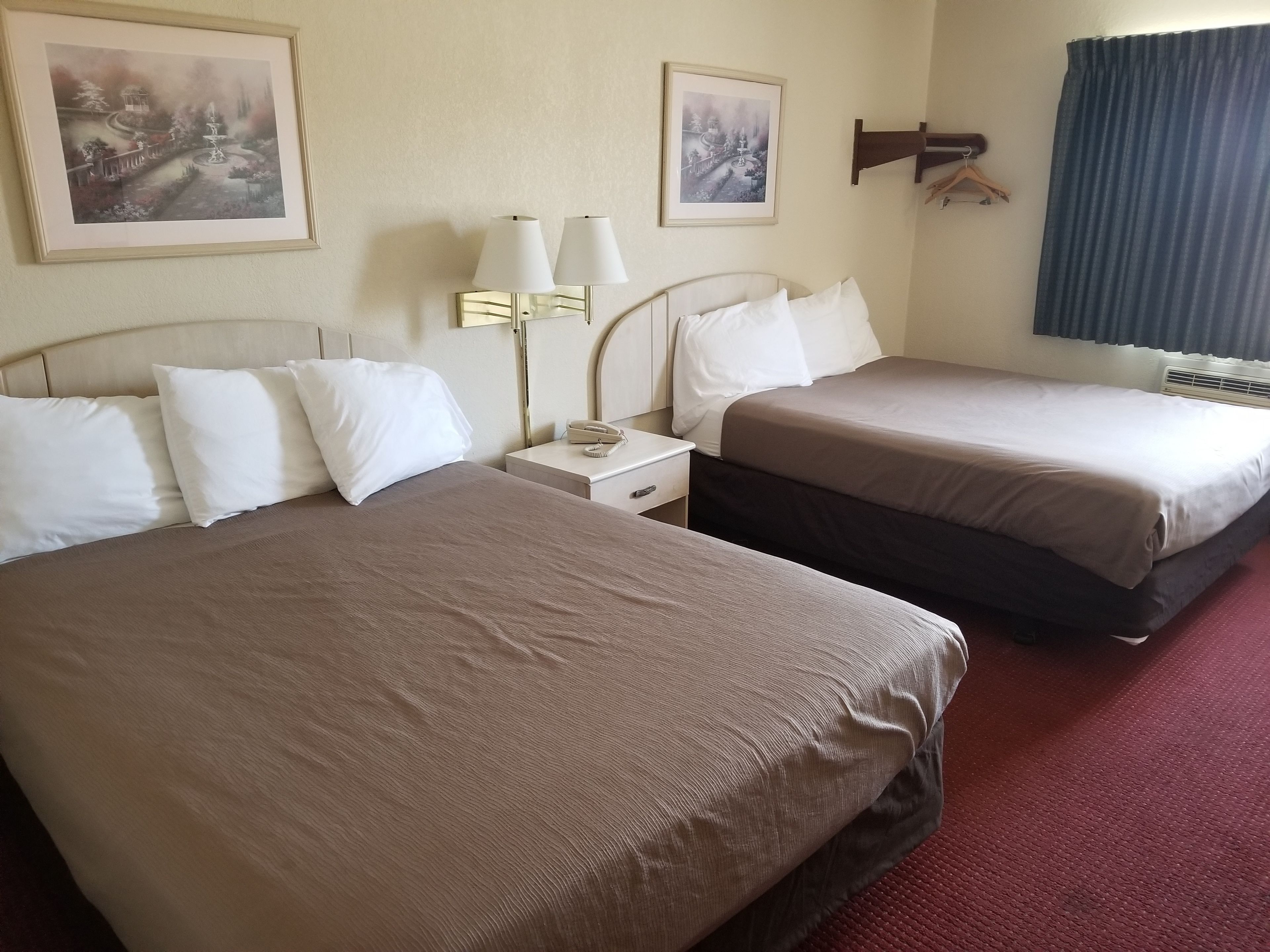 A hotel room with two beds, a nightstand with a lamp, and two framed pictures on the wall.