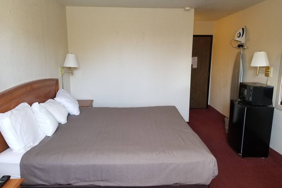 A hotel room with a large bed, two bedside lamps, a TV on a stand, and a door leading to another room.