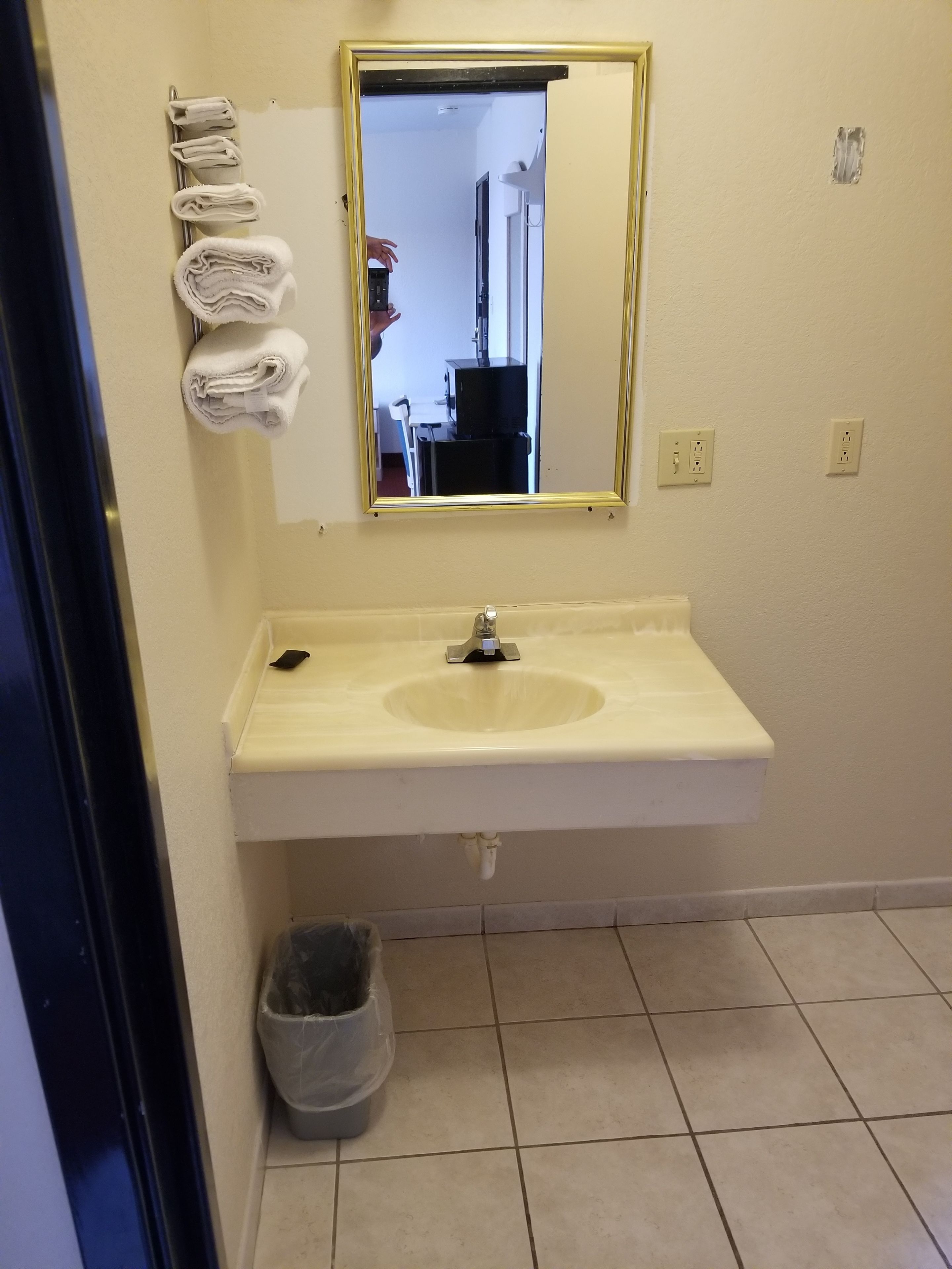 A bathroom with a sink, mirror, towel rack, and trash can.