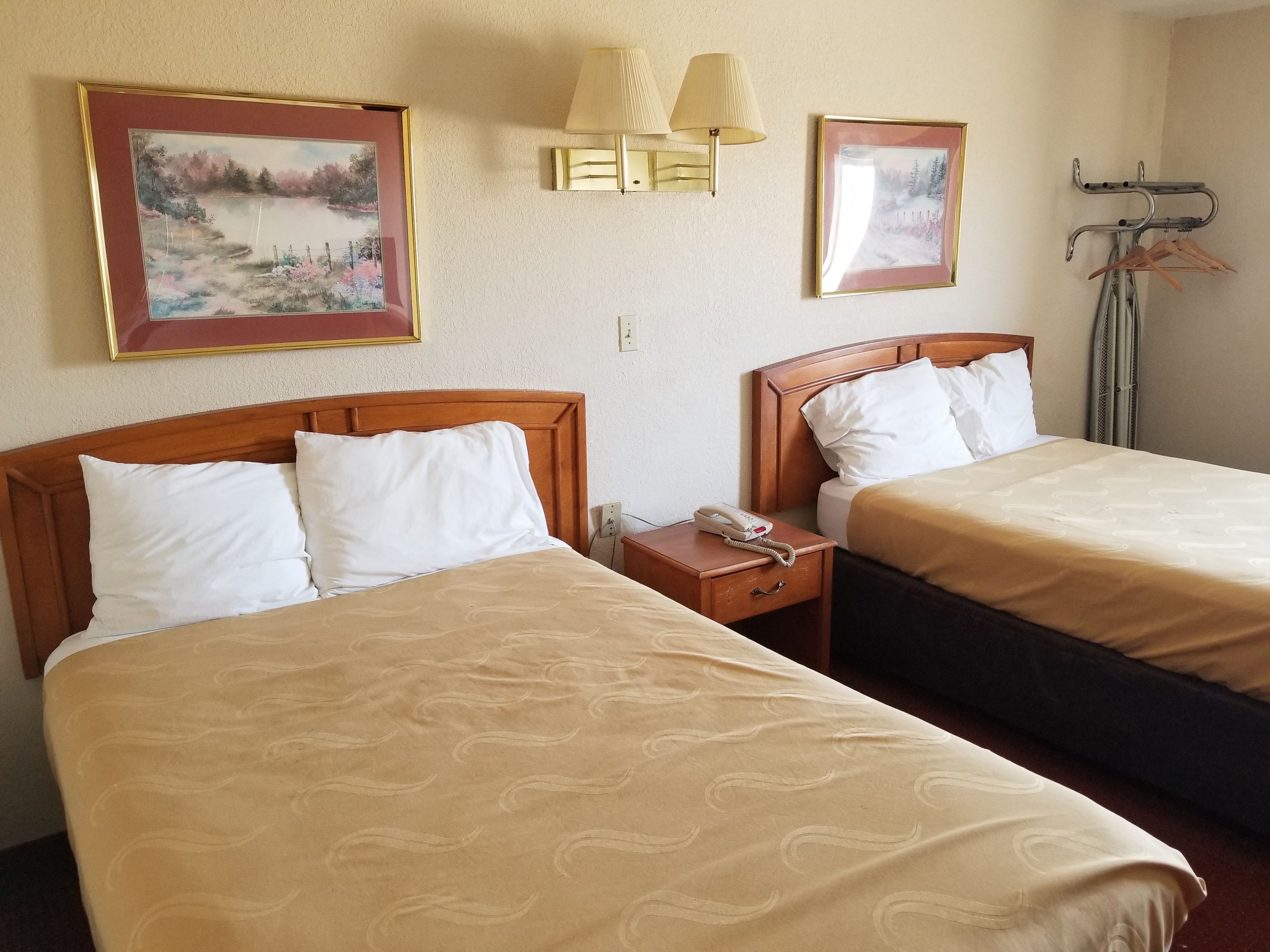 Two single beds with wooden headboards, beige bedding, a bedside table with a phone, and wall-mounted lamps.