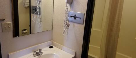 Un baño con lavabo, espejo, secador de pelo y cortina de ducha.