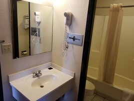 A bathroom with a sink, a mirror, a hairdryer, and a shower curtain.