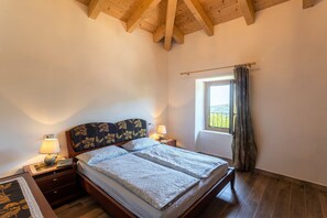 Un dormitorio con techo de madera, cama con cabecera floral, lámparas de noche y ventana con cortinas.