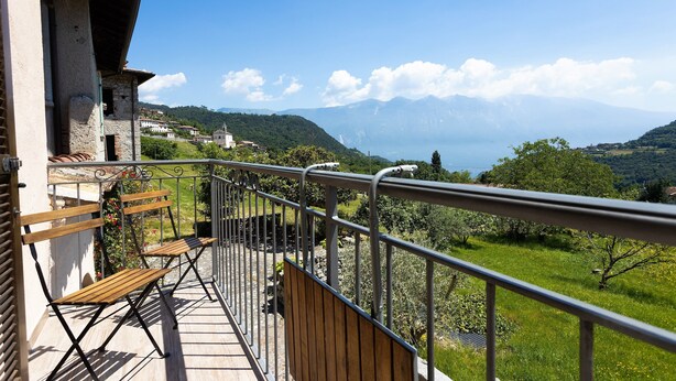Een balkon met een houten bankje, een leuning en uitzicht op een bergachtig landschap.