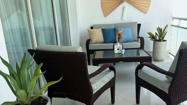 A modern living room with a glass partition, a sofa with cushions, a coffee table, two wicker chairs, and a potted plant. - Seawinds Cabarete Beachfront Penthouse, Stunning Balcony Views, Sleeps 6 (Cabarete)