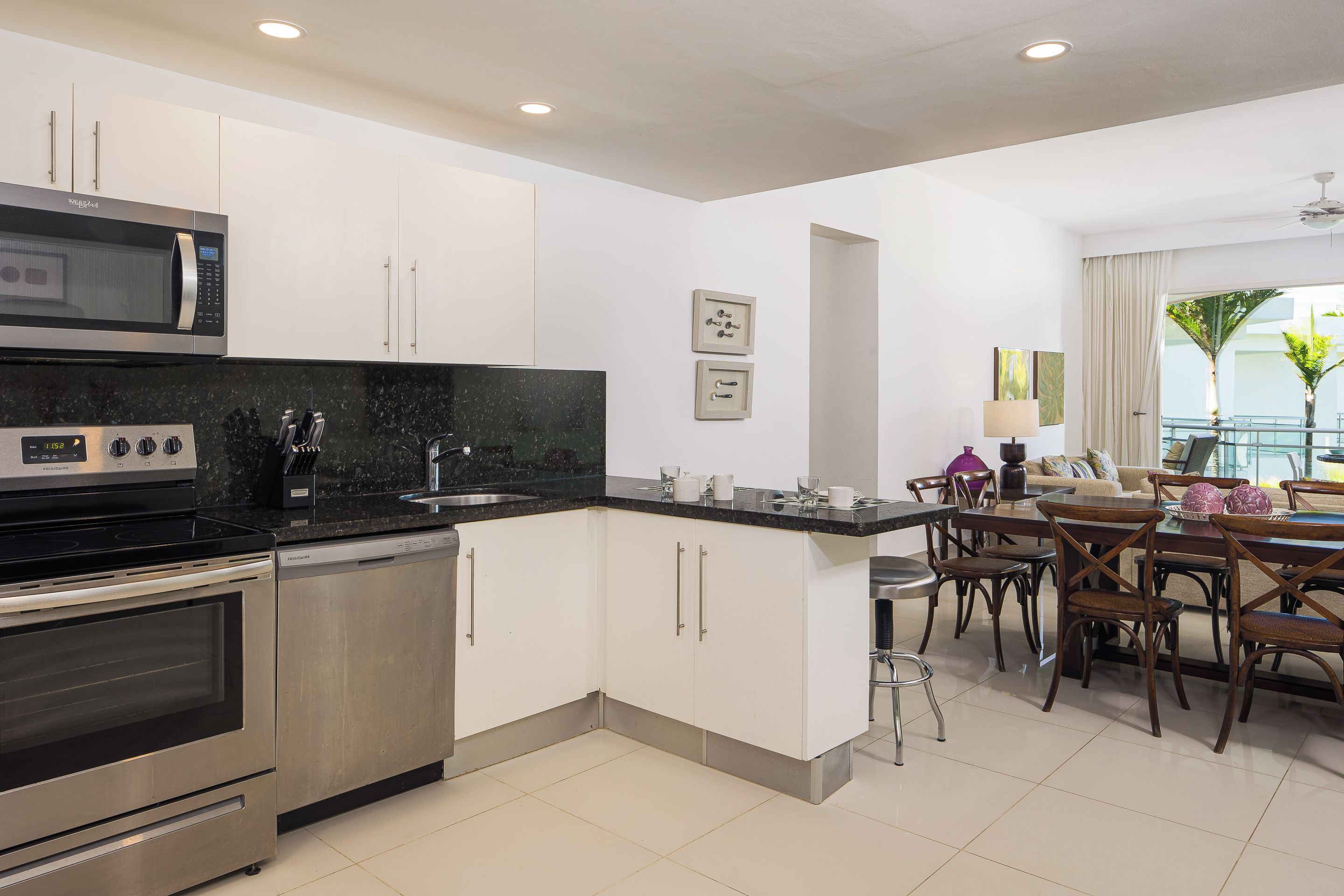 A modern kitchen with a built-in microwave, stove, and dishwasher, a dining area with a table and chairs, and a view of the outdoors through a window.