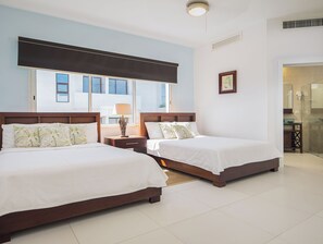 Een hotelkamer met twee bedden, een nachtkastje met een lamp, een raam met zonwering en een lijst met een afbeelding aan de muur.