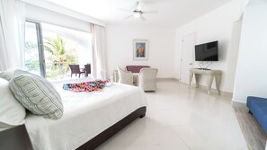 A hotel room with a bed, a TV, a balcony with chairs, and a painting on the wall. - Seawinds Cabarete Beachfront Penthouse, Stunning Balcony Views, Sleeps 6 (Cabarete)