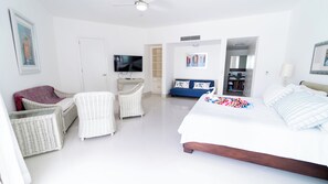 Ein Hotelzimmer mit einem Bett, zwei Korbstühlen, einem Sofa, einem Fernseher und einem durch eine geöffnete Tür einsehbaren Badezimmer.