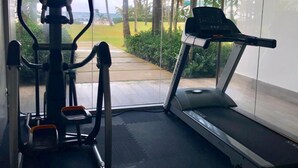 A gym with a treadmill and elliptical machine, a window with a view of palm trees and a pathway. - Seawinds Cabarete Beachfront Penthouse, Stunning Balcony Views, Sleeps 6 (Cabarete)