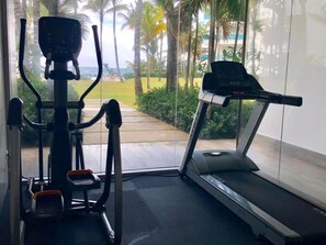 A gym with a treadmill and elliptical machine, a window with a view of palm trees and a pathway. - Seawinds Cabarete Beachfront Penthouse, Stunning Balcony Views, Sleeps 6 (Cabarete)