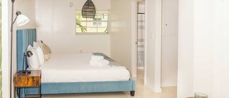 A bedroom with a bed, bedside table, lamp, and a view of the outside through a window.