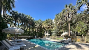 A swimming pool with lounge chairs and umbrellas, surrounded by palm trees and a fence. - Miami River Inn By Renzzi (Miami)