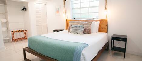Een slaapkamer met een bed, nachtkastjes, een kledingkast en een raam met natuurlijk licht.