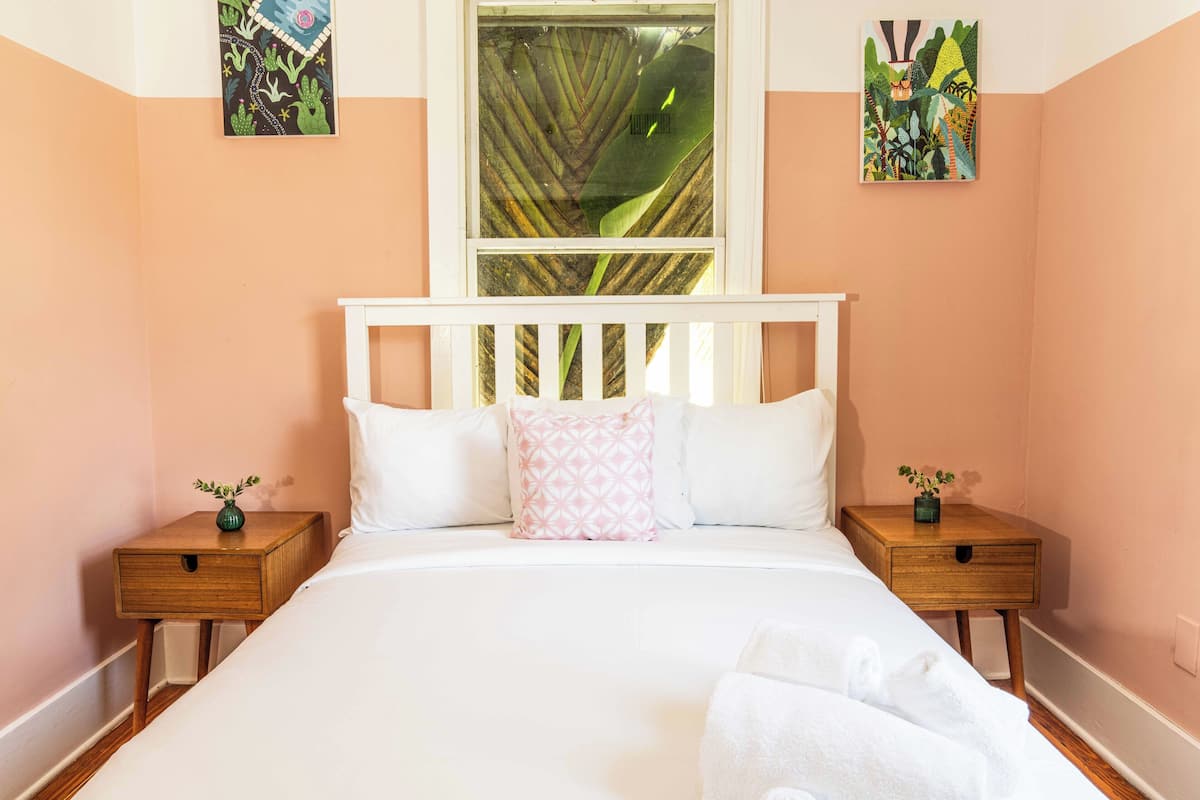 Een slaapkamer met een groot bed, twee nachtkastjes, een raam met uitzicht op een bos en twee aan de muur hangende kunstwerken.