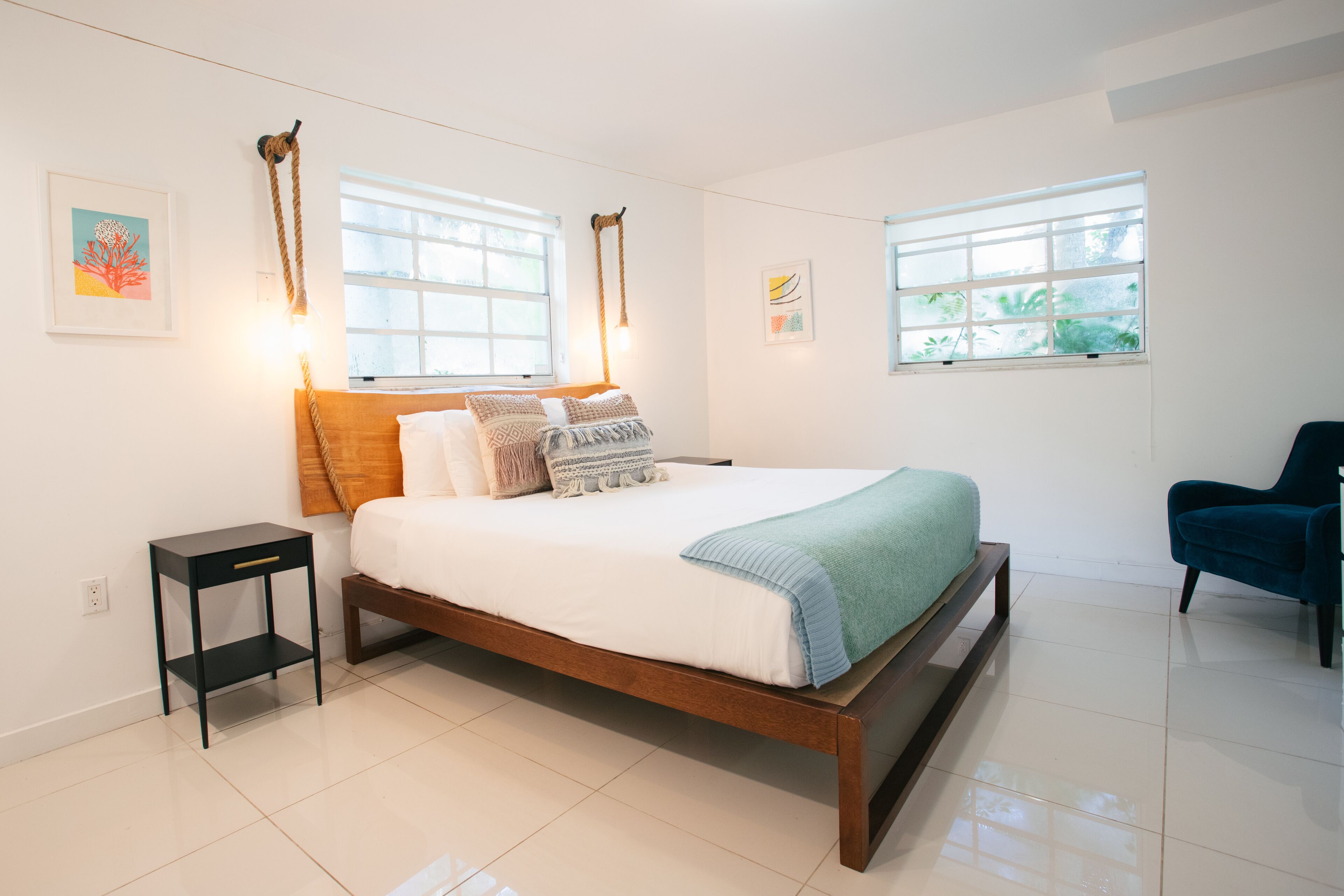 Une chambre à coucher moderne avec un lit en bois, des tables de chevet et deux fenêtres avec des rideaux.