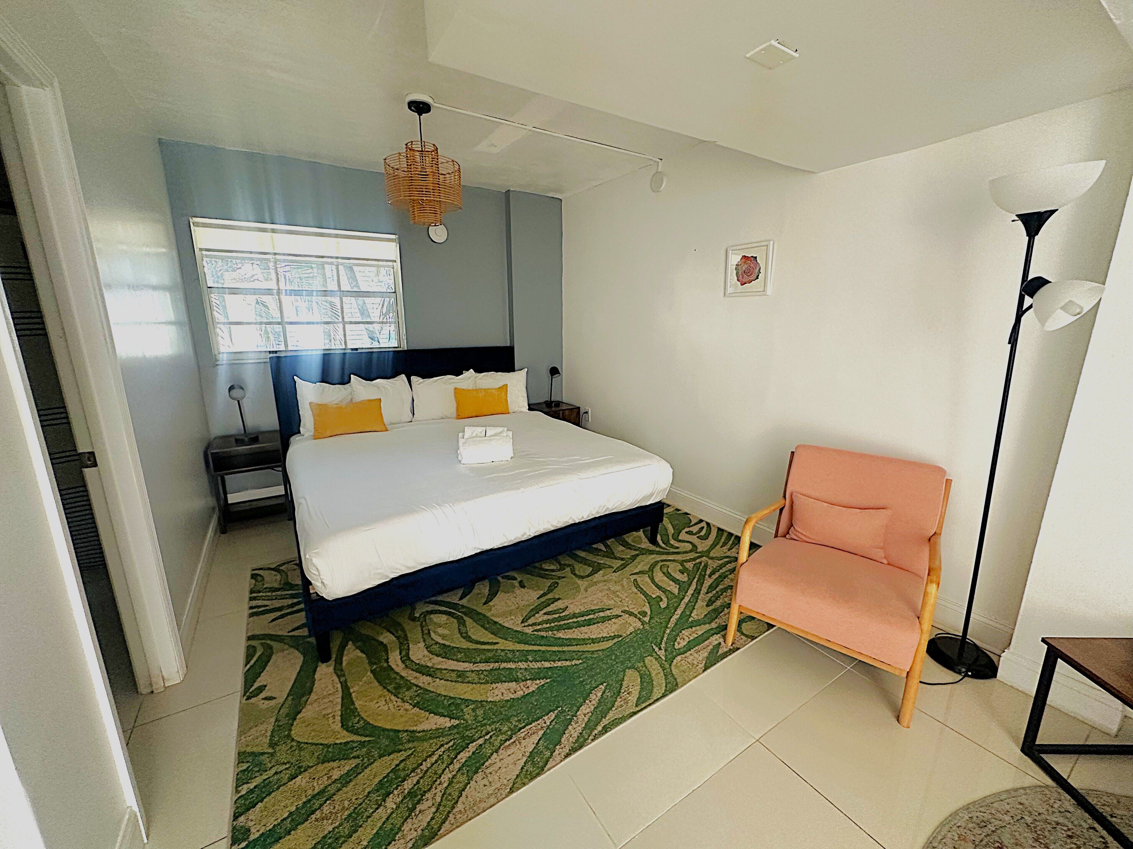 A hotel room with a bed, a chair, a nightstand, a lamp, and a window with a view.