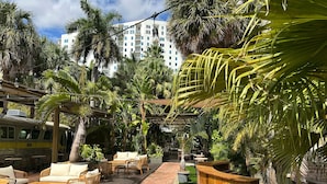 An outdoor patio area with wicker furniture, a wooden reception desk, and palm trees. - Miami River Inn By Renzzi (Miami)