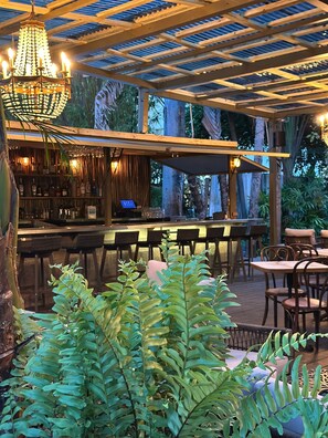 An outdoor bar area with a wooden pergola, bar stools, and a chandelier. - Miami River Inn By Renzzi (Miami)