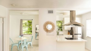 A modern kitchen with a central island, a dining area with light blue chairs, and a large window with a view of greenery. - Miami River Inn By Renzzi (Miami)