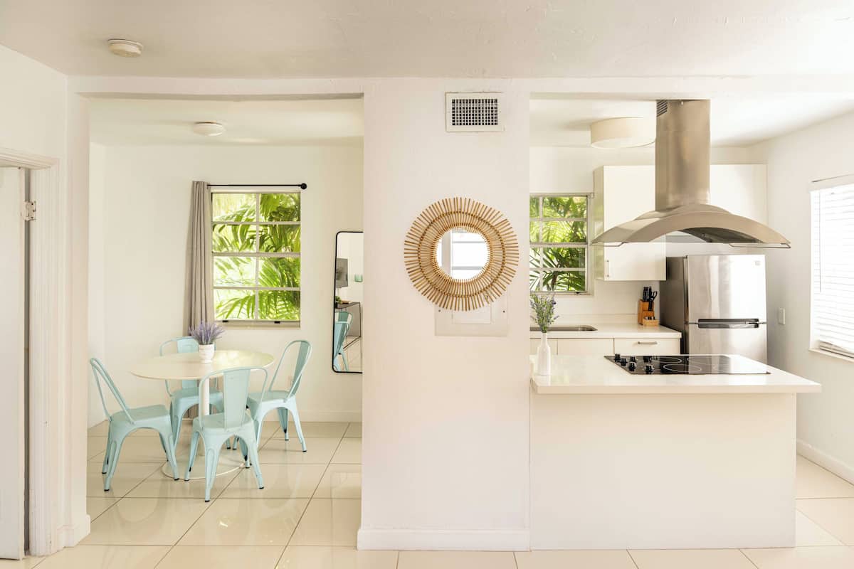 Een moderne keuken met een centraal eiland, een eethoek met lichtblauwe stoelen, en een groot raam met uitzicht op groen.