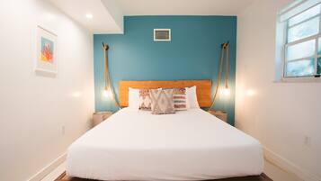 Une chambre à coucher avec une tête de lit en bois, une literie blanche et un mur d’accent bleu.