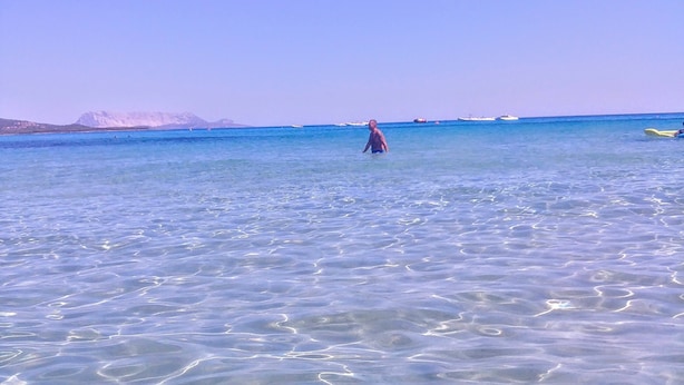 A clear view of a beach with calm waters and distant mountains.
