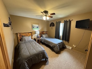 A bedroom with two beds, a ceiling fan, a TV, and a window with curtains.