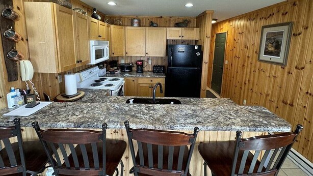 A kitchen with wooden cabinets, a granite countertop, a black refrigerator, and a sink. - 40 Creek Lodge North at Waubay Lake (Waubay)