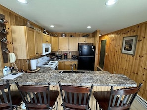 A kitchen with wooden cabinets, a granite countertop, a black refrigerator, and a sink.
