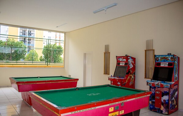A room with two pool tables, a window with a view of buildings, and two arcade machines.
