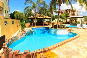 A swimming pool with a curved design, surrounded by palm trees and a covered seating area.
