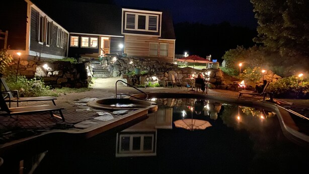 A nighttime view of a house with a swimming pool, stone steps, and outdoor seating.