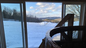 A room with a large sliding glass door leading to a snowy outdoor area with a view of trees and hills.