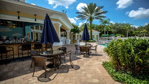 An outdoor patio area with wicker furniture, umbrellas, and a pool in the background.