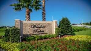 A sign for 'Windor Palms' with a stone facade and a landscaped garden with red flowers.