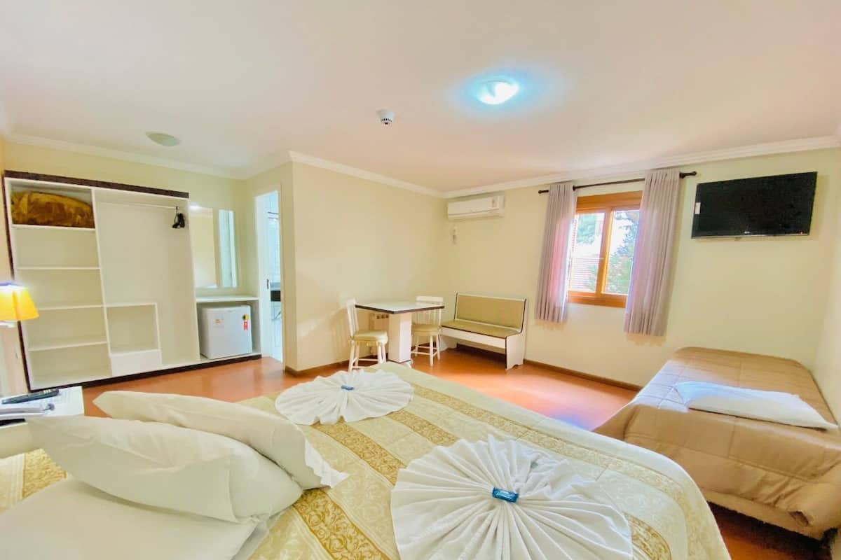 Quarto de hotel com cama, sofá, mesa de jantar e cozinha compacta.