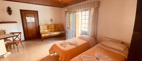 A room with two beds, a desk, a chair, a bench, and a window with curtains.