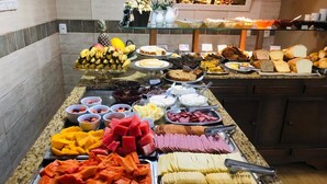 A buffet with various food items including fruits, vegetables, and meats. - Zermatt Hotel (Gramado)