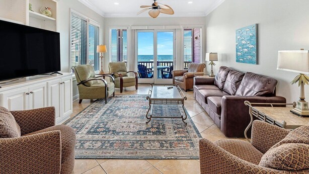 A spacious living room with a large flat-screen TV, comfortable seating, a patterned rug, and a view to the outside.