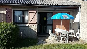 A house with a patio area featuring a table and chairs, a blue umbrella, and a wooden door.